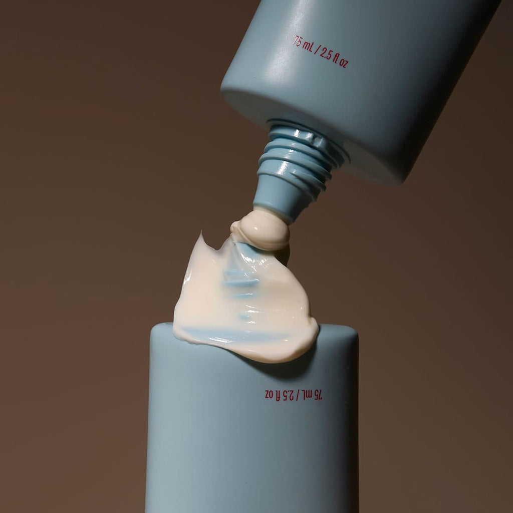 Close-up of a blue bottle being filled with white cream against a brown background.