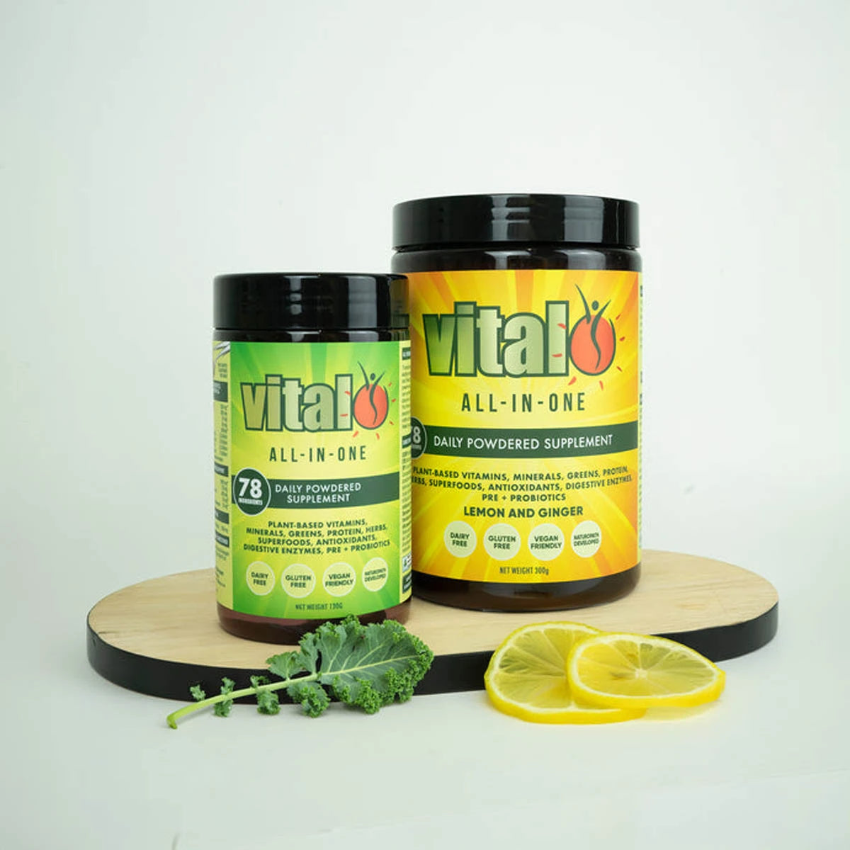 Two 'vital all-in-one' supplement containers on a wooden stand with lemon slices and kale leaves.