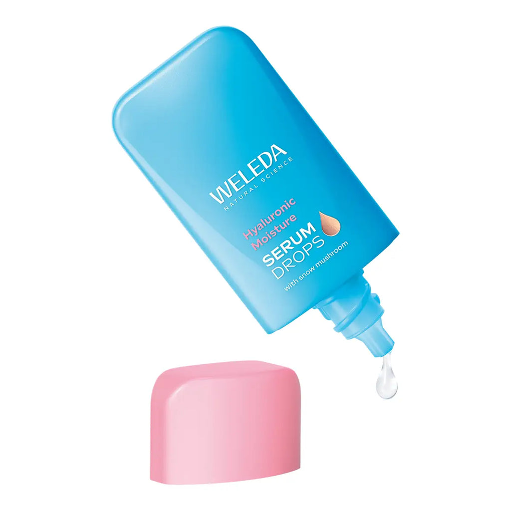 A blue bottle of Weleda Hyaluronic Moisture Serum Drops with its pink cap placed below it on a white background.