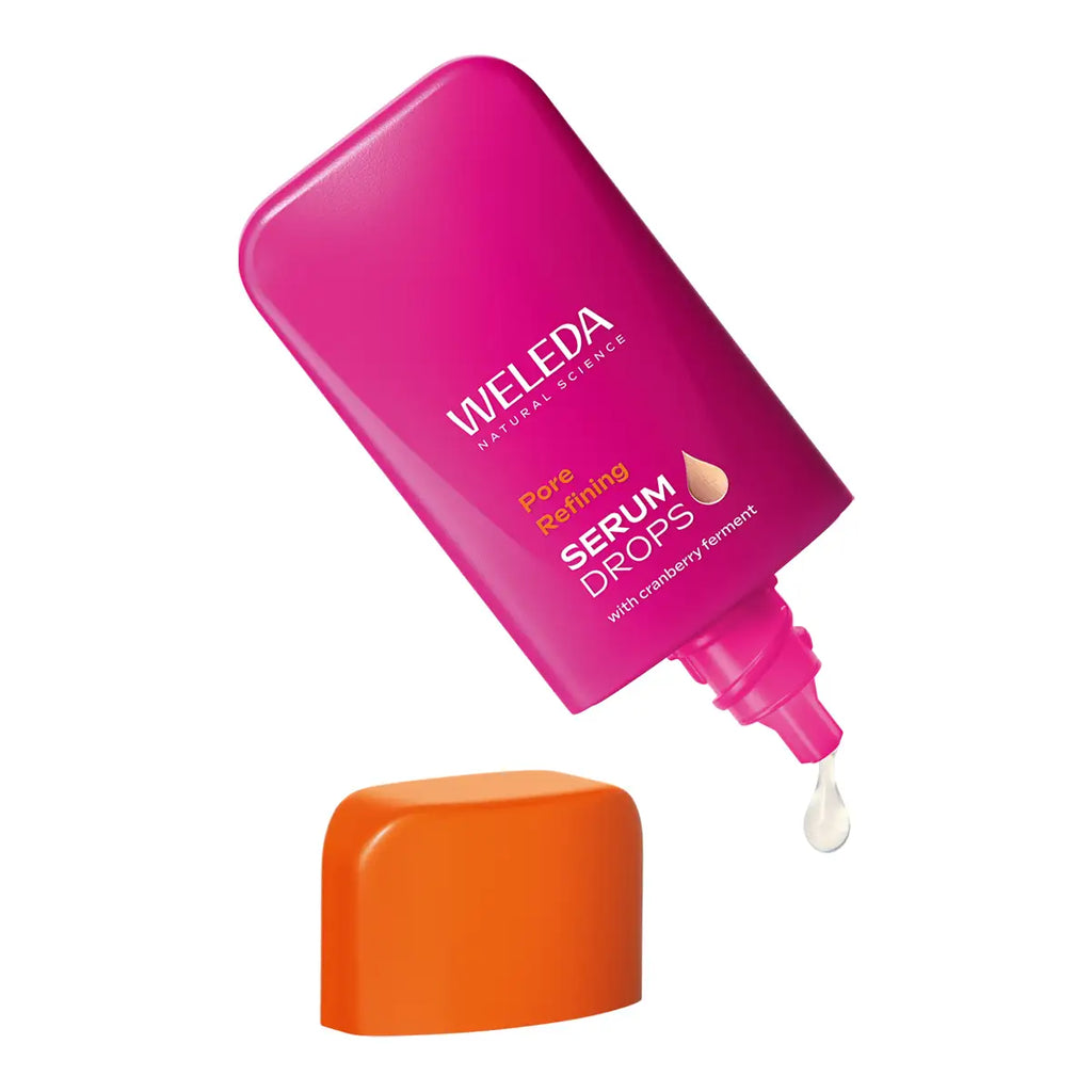 A bottle of Weleda Pore Refining Serum Drops in a vibrant magenta pink color, shown tilted with its bright orange cap resting below.